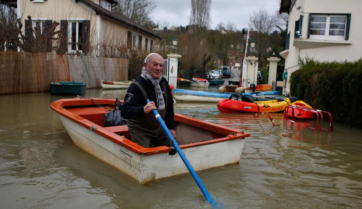 Seorang pria menggunakan perahu di jalan banjir di pulau Vaux, sebelah barat Paris, (30/1). Meluapnya sungai Seine di Paris membuat kebun dan jalan terendam banjir. (AP Photo / Thibault Camus)