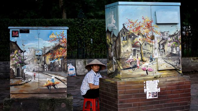 Pedagang menunggu pelanggan sambil duduk di belakang kotak listrik yang dihiasi lukisan di Hanoi, ibu kota Vietnam pada 11 Agustus 2020. Setelah mencatat nol kasus COVID-19 selama lebih dari tiga bulan, Vietnam melaporkan sejumlah infeksi baru di dalam negeri sejak akhir Juli. (MANAN VATSYAYANA/AFP)