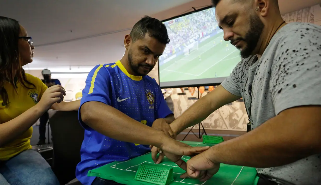 Suporter Brasil yang buta dan tuli, Carlos Junior merasakan berlangsungnya pertandingan 16 besar Piala Dunia 2018 antara Brasil melawan Meksiko dibantu penerjemah dengan miniatur lapangan sepak bola di Sao Paulo, Brasil, (2/7). (AP Photo / Nelson Antoine)