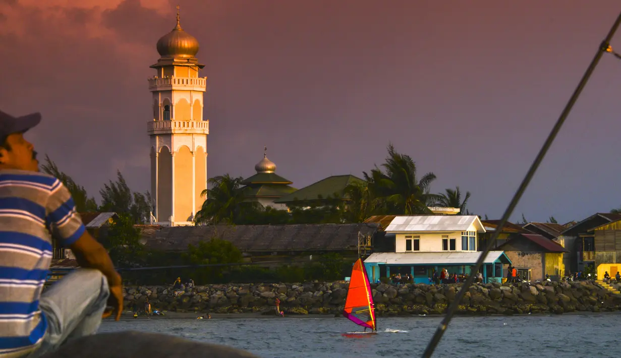 Seorang pria memancing ketika pemain selancar angin melintas saat matahari terbenam di pantai di Banda Aceh (7/4). Sebagai pusat pemerintahan, Banda Aceh menjadi pusat kegiatan ekonomi, politik, sosial dan budaya. (AFP Photo/Chaideer Mahyuddin)
