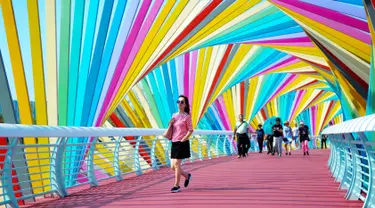 Warga berjalan melintasi jembatan warna-warni seperti pelangi yang berada di Qingdao, Shandong, China, Kamis (6/9). Jembatan pelangi ini terletak di Tangdaowan Seaside Park. (STR/AFP)