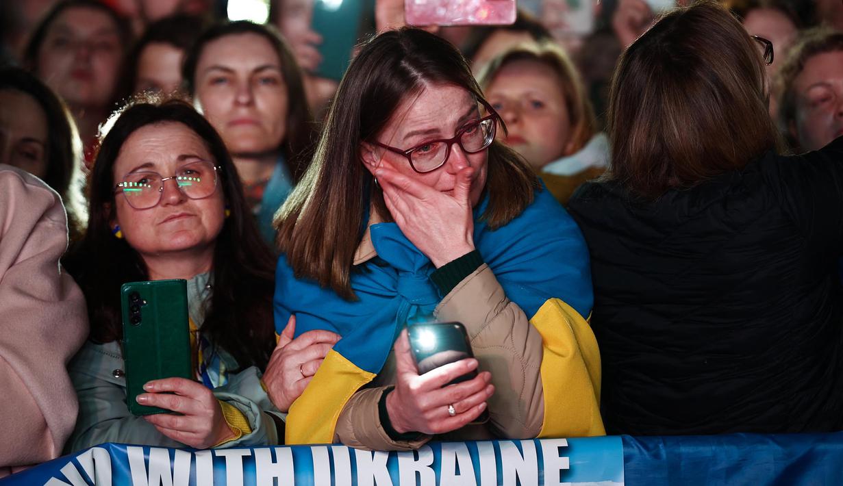 Seorang pengunjuk rasa berbalut bendera nasional Ukraina bereaksi ketika ia mengambil bagian dalam pertemuan untuk mendukung Ukraina yang menandai tahun ketiga invasi Rusia di Trafalgar Square, pusat kota London, pada 24 Februari 2025. (HENRY NICHOLLS/AFP)