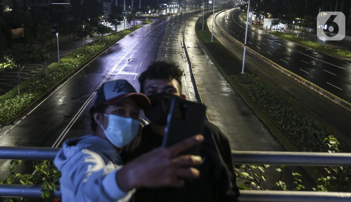 Warga berswafoto saat diberlakukannya Car Free Night dan Crowd Free Night di Jalan Sudirman-MH Thamrin, Jakarta (31/12/2020). Jalan Sudirman-MH Thamrin ditutup pada malam pergantian tahun untuk mencegah kerumunan warga. (Liputan6.com/Johan Tallo)