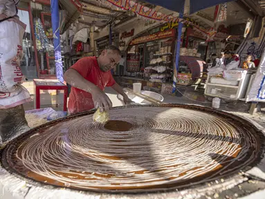 Pembuat penganan Mesir Mostafa Anwar membuat makanan penutup tradisional yang disebut "Kunafa" sebelum berbuka puasa, di kiosnya di ibu kota Kairo pada 14 April 2022.  Kunafa merupakan hidangan pencuci mulut utama di kalangan orang Arab selama Ramadhan berlangsung. (Khaled DESOUKI/AFP)