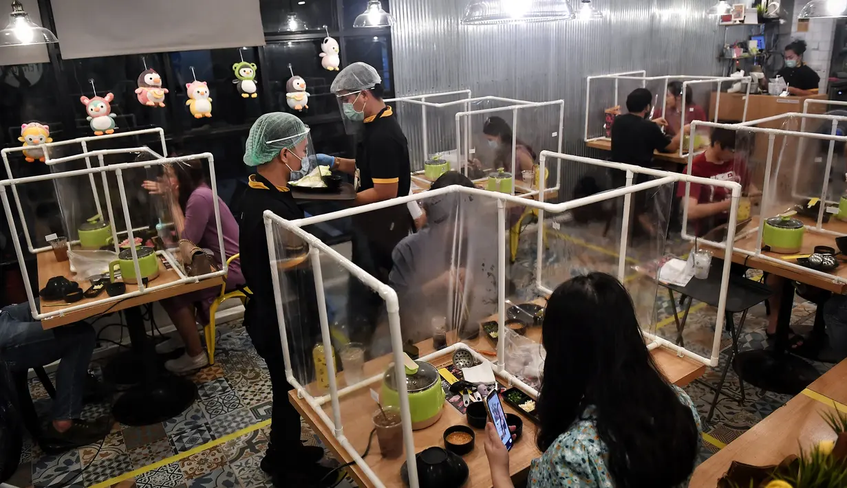 Pengunjung makan di sela-sela pembatas plastik untuk mencegah penyebaran virus corona di restoran hotpot Penguin Eat Shabu di Bangkok, 5 Mei 2020. Restoran kembali dibuka setelah Thailand memperlonggar lockdown dengan mengizinkan tempat makan menerapkan social distancing. (Lillian SUWANRUMPHA/AFP)