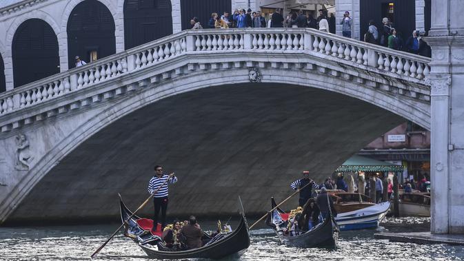 Gondola mengangkut wisatawan di sepanjang Grand Canal di bawah jembatan Rialto di Venesia (4/11/2019). Republik Venesia berdiri di kota ini dari abad ke-9 hingga ke-18. (AFP Photo/Miguel Medina)