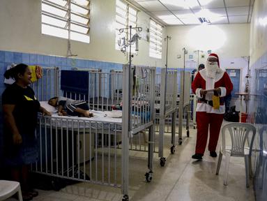 Seorang pria berpakaian seperti Sinterklas berjalan menyusuri lorong untuk mengantarkan hadiah kepada anak-anak yang dirawat di ruang gawat darurat sebuah rumah sakit di lingkungan El Cementerio di Caracas, Venezuela pada 25 Desember 2023. (Pedro Rances Mattey / AFP)