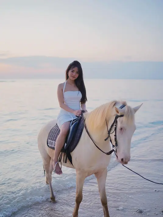 Manisnya penampilan Fuji naik kuda di pantai. Ia mengenakan halter neck dress berwarna putih yang membalut tubuhnya dengan amat apik. [Foto: Instagram/fuji_an]
