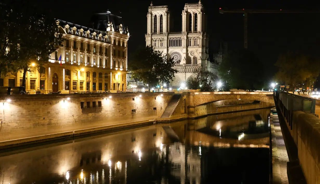 Pandangan umum dari Katedral Notre Dame tercermin di sungai Seine pada malam hari selama penerapan lockdown atau penguncian wilayah di Paris, 23 April 2020. Pandemi corona COVID-19 membuat Prancis menerapkan lockdown. (Ludovic MARIN / AFP)