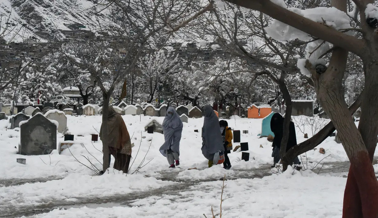 Sejumlah orang berjalan melewati makam usai hujan salju lebat di Quetta, Pakistan, Senin (13/1/2020). Cuaca buruk berupa hujan salju lebat, hujan, dan banjir bandang melanda Pakistan dan Afghanistan. (Banaras KHAN/AFP)