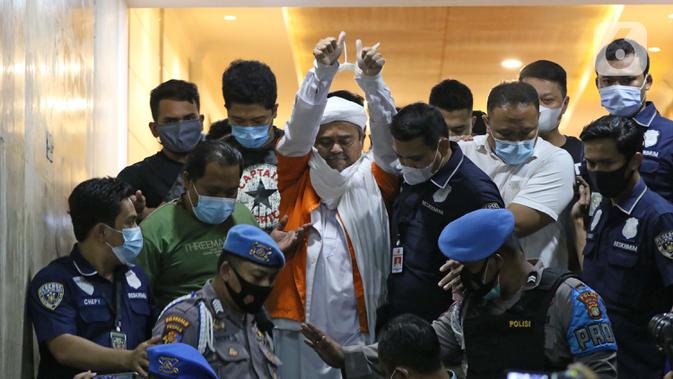 M Rizieq Shihab (tengah) digiring petugas saat meninggalkan gedung Ditreskrimum Polda Metro Jaya, Jakarta, Minggu dini hari (13/12/2020). Rizieq Shihab ditahan setelah menjalani pemeriksaan sebagai tersangka penghasutan dan kerumunan di tengah pandemi COVID-19. (Liputan6.com/Helmi Fithriansyah)