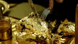 Seniman Prancis, Frederique Lecerf membungkus ayam dengan lembaran emas tipis 24 karat dalam acara makan malam di Paris, 28 Maret 2019. Lembaran tipis emas menyelimuti makanan sederhana seperti ayam, telur rebus, dan kue-kue berlapis emas untuk pencuci mulut. (REUTERS/Philippe Wojazer)