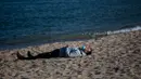 Seorang pria mengenakan masker beristirahat ketika penguncian untuk memerangi penyebaran virus corona berlanjut di sebuah pantai di Badalona, dekat Barcelona, Spanyol, Selasa, (28/4/2020). (AP Photo/Emilio Morenatti)