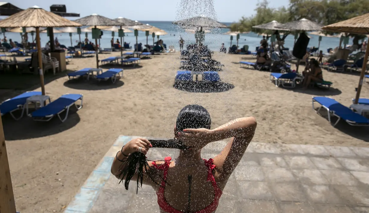 Seorang wanita mandi di pantai Desa Lagonissi, beberapa mil barat daya Athena, Yunani, Kamis (29/7/2021). Gelombang panas membuat orang-orang berbondong-bondong ke pantai, air mancur umum, dan lokasi ber-AC. (AP Photo/Yorgos Karahalis)