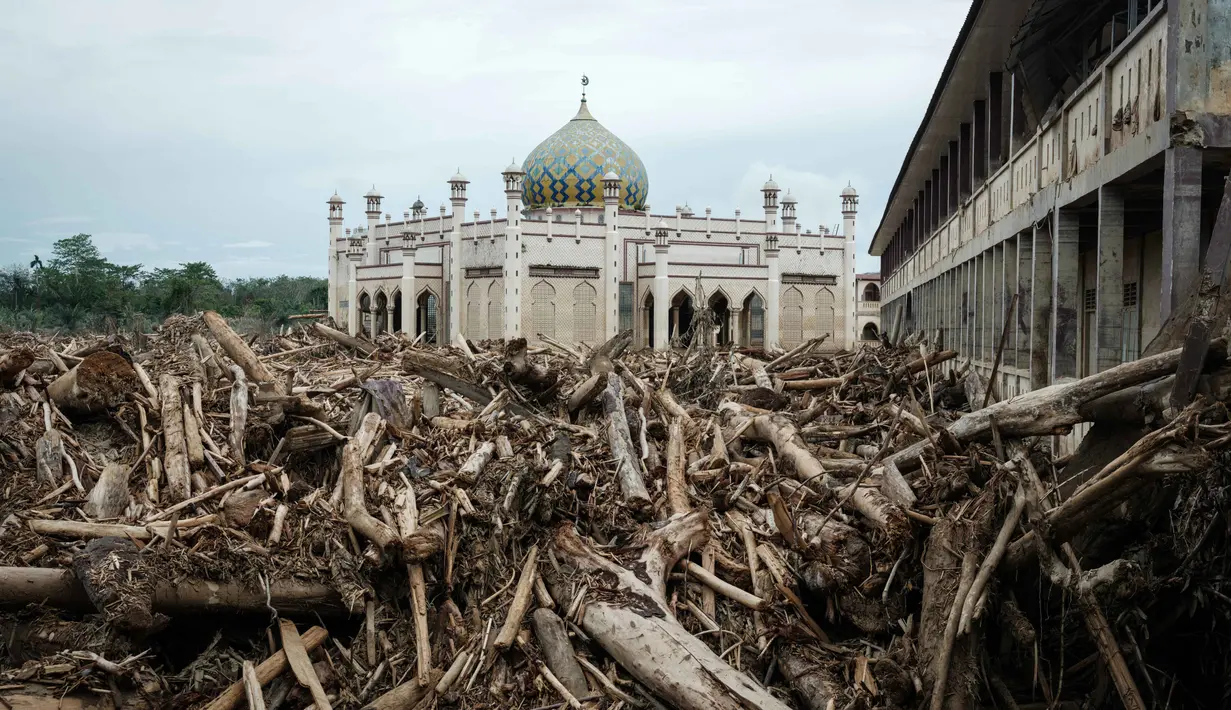 Ruang-ruang belajar serta pondokan tempat para santri menginap masih utuh, meski terkubur lumpur dan tumpukan kayu di bagian lantai satu. Tampak dalam foto, tumpukan pohon tumbang yang tersapu banjir bandang sekitar tiga minggu lalu masih terlihat di Pesantren Darul Mukhlisin dan masjid yang terhubung dengan pesantren tersebut di Aceh Tamiang, pada Minggu 14 Desember 2025. (Yasuyoshi CHIBA/AFP)