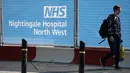 Pejalan kaki melewati papan penanda di pusat konferensi Manchester Central yang menjadi rumah sakit lapangan bernama NHS Nightingale Hospital North West untuk membantu memerangi COVID-19 di Manchester, 13 April 2020.. Rumah sakit itu dapat menampung hingga 750 pasien. (Xinhua/Jon Super)