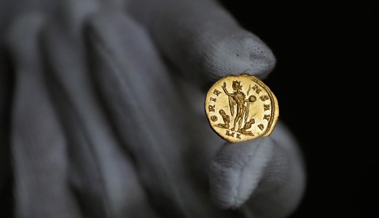 Seorang karyawan Dix Noonan Webb menunjukkan koin Romawi kuno di London, Inggris (28/5/2019). Koin emas ini berasal dari tahun 293-296 M yang ditemukan di sebuah lapangan di Kent, Inggris. (AP Photo/Kirsty Wigglesworth)