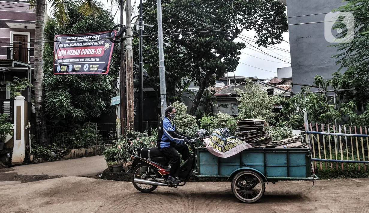 Warga berjalan di dekat spanduk peringatan Zona Merah di RW 004, Kelurahan Cipinang Melayu, Kecamatan Makassar Jakarta, Rabu (27/1/2021). Pemprov DKI Jakarta mencatat sebanyak 54 rukun warga (RW) menjadi zona merah Covid-19 per 21 Januari 2021. (merdeka.com/Iqbal S Nugroho)