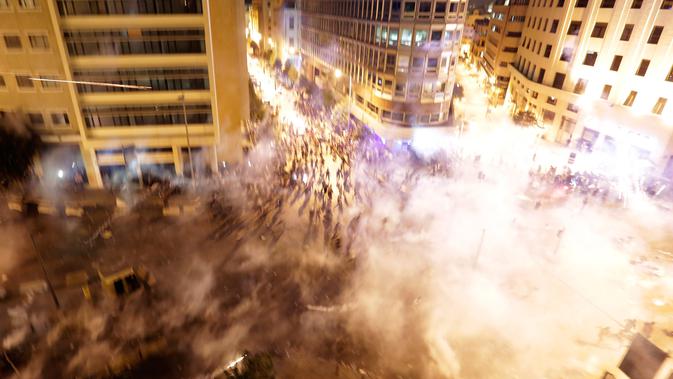 Pengunjuk rasa berlarian saat polisi menembakkan gas air mata untuk membubarkan massa selama protes menentang rencana pengenaan pajak baru di Beirut, Lebanon, Jumat (18/10/2019). Saat ini Lebanon menjadi salah satu negara dengan utang terbesar di dunia. (AP Photo/Hassan Ammar)
