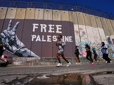 Para pelari melewati tembok pemisah Israel saat mereka berkompetisi dalam Maraton Palestina di kota Betlehem, Tepi Barat, Jumat 8 Mei 2026. Maraton Internasional Palestina kembali dilaksanakan pada Jumat 8 Mei 2026, di kota Betlehem, Tepi Barat. (AP Photo/Mahmoud Illean)