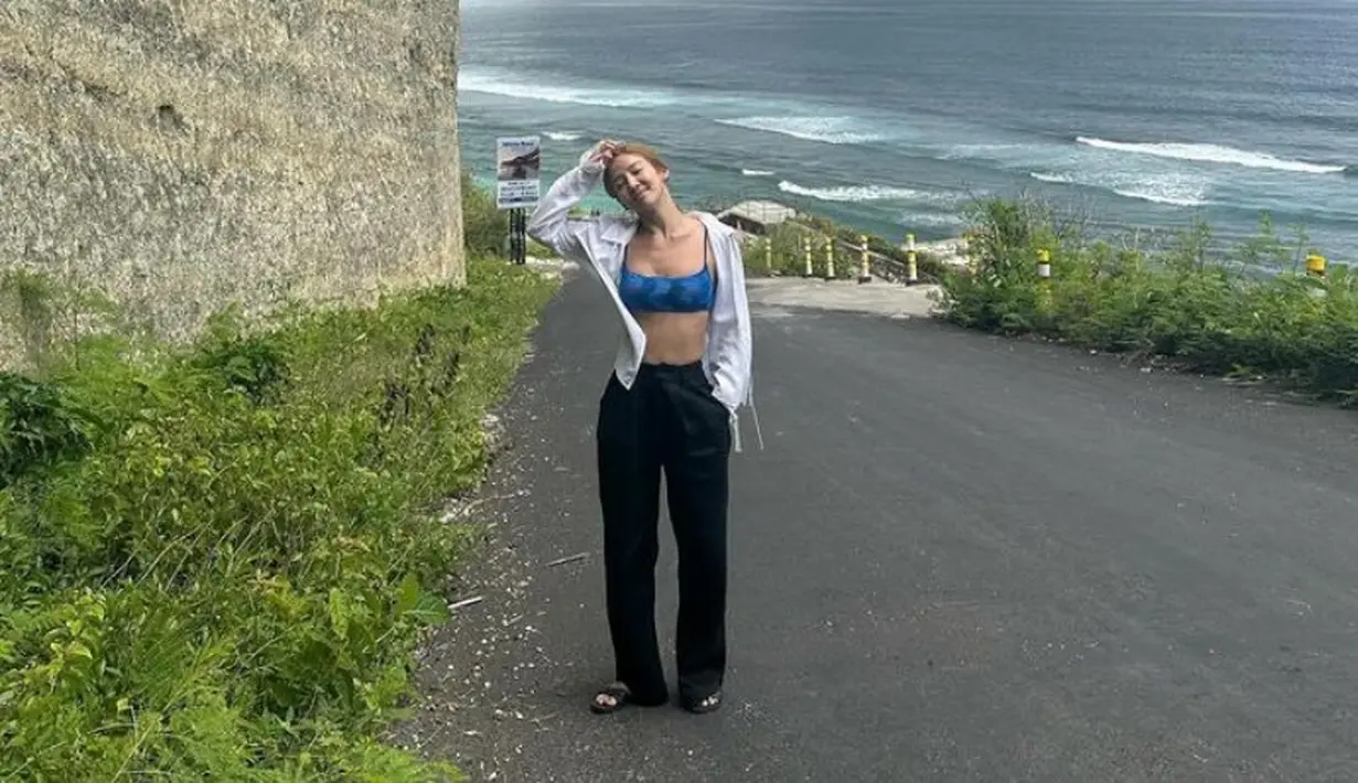 Hyoyeon berada di Bali, saat di pantai ia pun mengenakan bra top biru dipadukan outer kemeja putih dan celana panjang hitam. [@hyoyeon_x_x]
