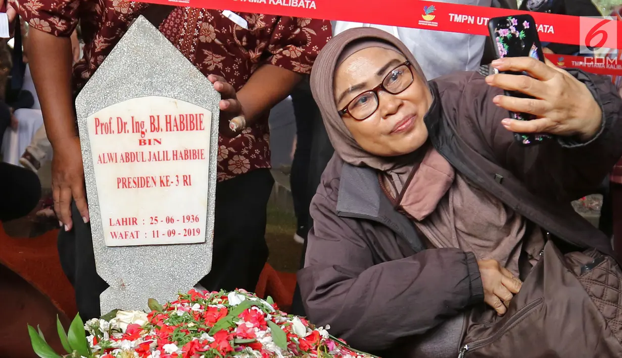 Seorang wanita berswafoto dengan latar belakang batu nisan Presiden ketiga BJ Habibie di Taman Makam Pahlawan Nasional Kalibata, Jakarta, Kamis (12/9/2019). Selain berdoa, tidak sedikit juga warga  mengabadikan dengan kamera ponsel. (Liputan6.com/Herman Zakharia)