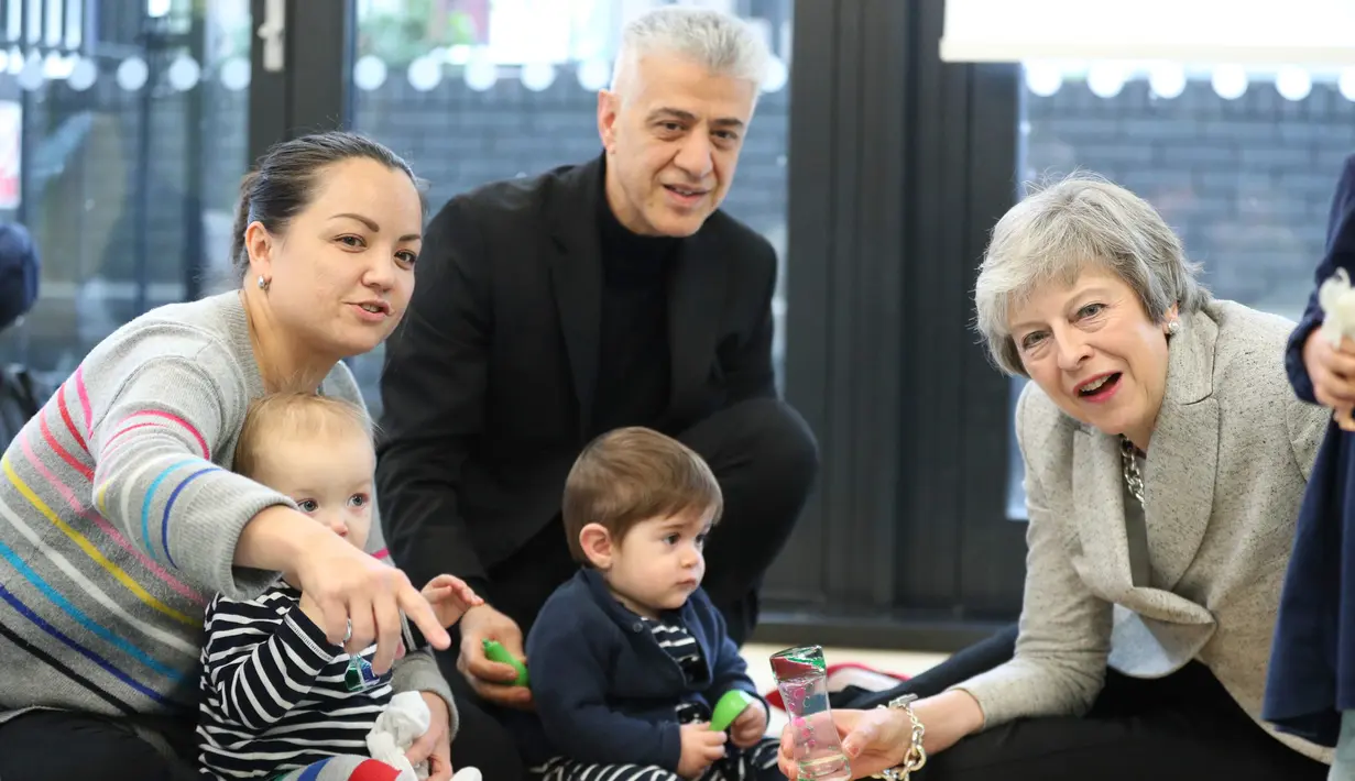 Ekspresi Perdana Menteri Inggris Theresa May saat bermain dengan bayi di pusat kesehatan di London, Inggris, Kamis (22/11). Theresa menjadi PM Inggris setelah David Cameron, PM sebelumnya, mengundurkan diri akibat Brexit. (Andrew Matthews/Pool via AP)