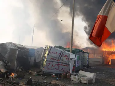 Sebuah bendera Prancis berada di dekat Kobaran api yang membakar sebuah kamp pengungsian imigran selama pembongkaran kamp pengungsian imigran "Jungle", di kota pelabuhan Calais, Prancis (26/10). (REUTERS/Pascal Rossignol)