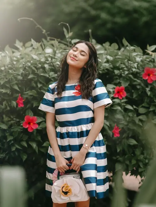 Penampilan memesona Azizah Salsha pakai dress bercorak garis-garis biru dan putih dengan detail corak bunga merah di salah satu sisi dadanya. [Foto: Instagram/azizahsalsha_]