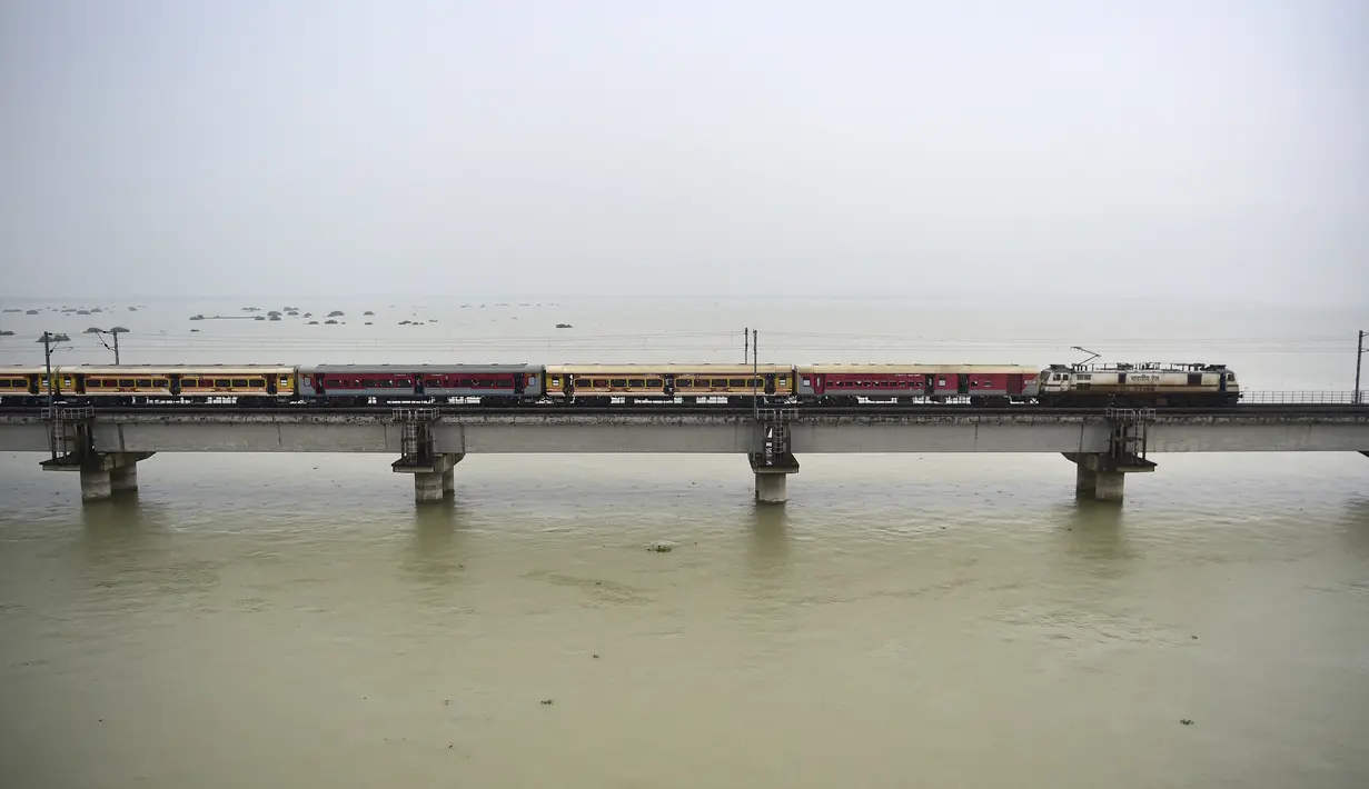 Sebuah kereta penumpang melintasi jembatan di atas Sungai Gangga yang banjir di Allahabad, India, Rabu (11/8/2021). Hujan lebat menyebabkan permukaan air Sungai Gangga dan Yamuna naik sehingga terjadi banjir. (SANJAY KANOJIA/AFP)