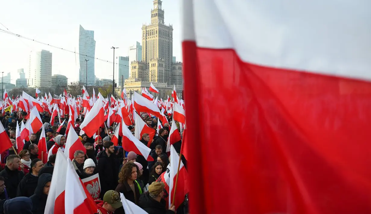 Orang-orang mengibarkan bendera nasional Polandia saat pawai untuk menandai Hari Kemerdekaan Nasional Polandia di Warsawa, Polandia, 11 November 2021. Hari Kemerdekaan Nasional Polandia dirayakan pada 11 November untuk memperingati ulang tahun Republik Polandia Kedua. (Adam Chelstowski/AFP)