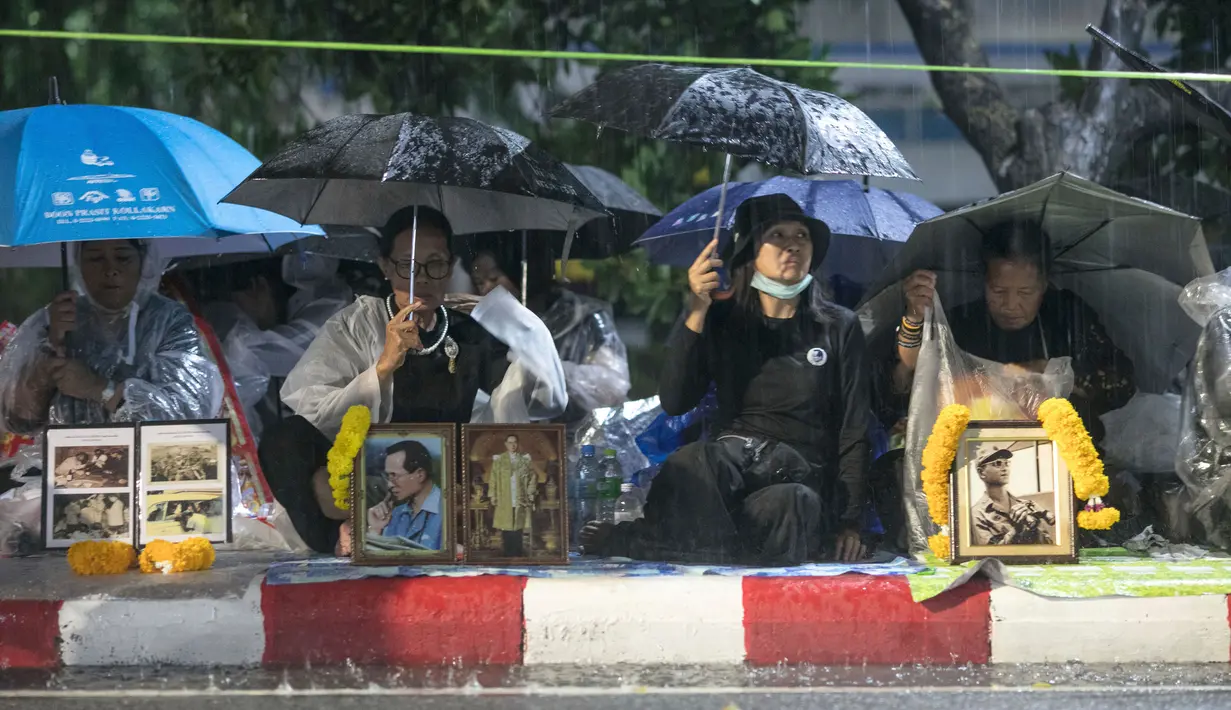 Pelayat menggunakan payung sambil menunggu hujan demi menghadiri upacara kremasi Raja Thailand Bhumibol Adulyadej di Bangkok, Selasa (24/10). Prosesi kremasi Raja Bhumibol dilaporkan telah menelan biaya hingga sekitar Rp1,2 triliun. (AP/Wason Wanichakorn)