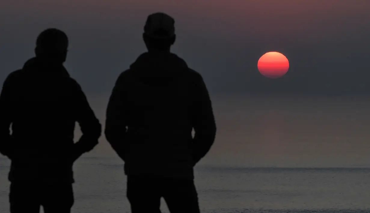 Dua pria melihat matahari terbenam di Cap Frehel, di Plevenon, Prancis barat (26/2). Semenanjung ini dikelilingi oleh tebing-tebing, yang membuatnya sulit diakses melalui laut. (AFP Photo/Loic Venance)
