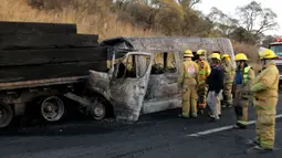 Petugas pemadam kebakaran berada di lokasi kecelakaan antara sebuah van dan truk kargo  di jalan raya Negara Bagian Jalisco, Meksiko, Rabu (18/12/2019). Sebuah van yang membawa keluarga untuk liburan di pantai menabrak truk bermuatan kayu yang sedang terparkir di sisi jalan raya. (Ulises Ruiz / AFP)