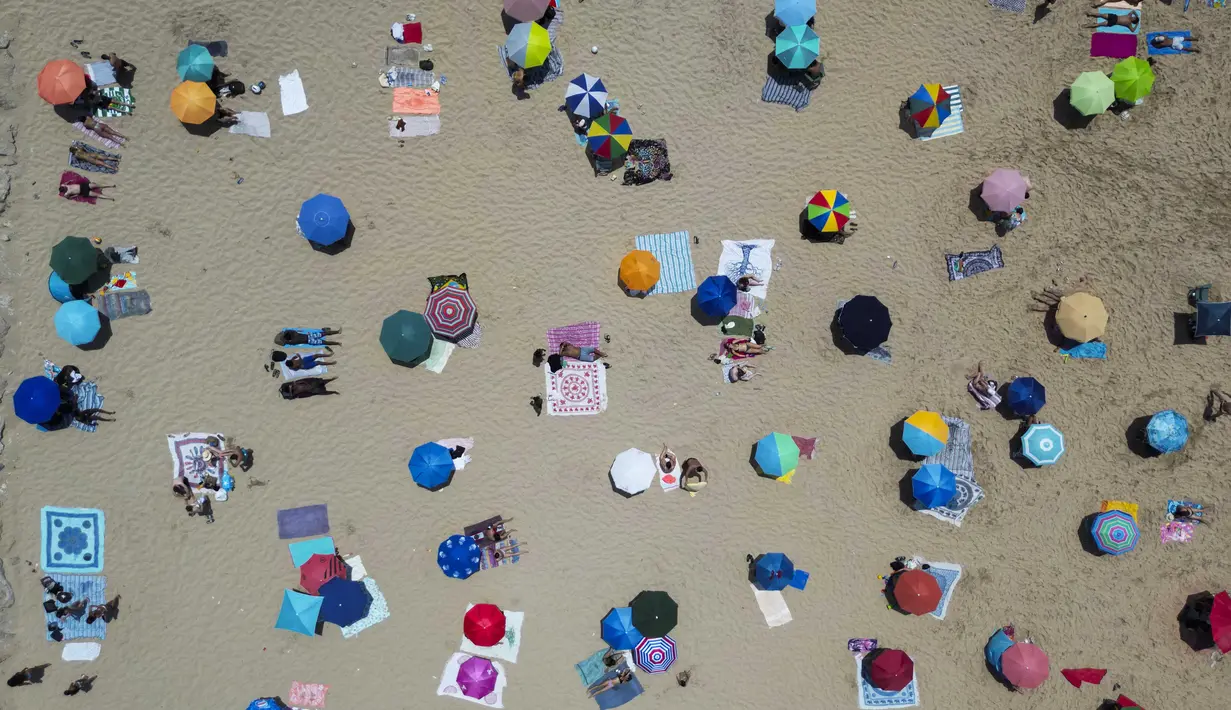 Foto udara menunjukkan orang-orang berjemur di pantai Costa da Caparica di Almada, dekat Lisbon, selama gelombang panas pertama tahun ini, pada tanggal 29 Juni 2025. (CARLOS COSTA/AFP)