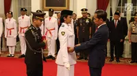 Presiden Joko Widodo (kanan) memasangkan kendit kepada perwakilan anggota Pasukan Pengibar Bendera Pusaka (Paskibraka) saat pengukuhan di Istana Negara, Jakarta, Kamis (15/8/2019). Sebanyak 68 anggota Paskibraka tersebut akan bertugas pada upacara HUT ke-74 RI. (Liputan6.com/Angga Yuniar)