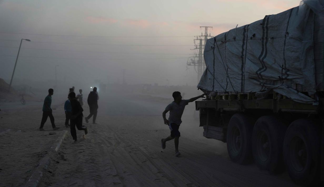 Dalam keterangan resminya, pada Sabtu (8/11/2025), OCHA mengatakan penyaluran bantuan masih dibatasi hanya melalui dua pos perlintasan saja. Tampak dalam foto, warga Palestina berbondong-bondong menuju truk yang mengangkut bantuan dari Program Pangan Dunia (WFP) saat truk-truk tersebut melintasi Deir al-Balah di Gaza Tengah, Sabtu, 8 November 2025. (AP Photo/Abdel Kareem Hana)