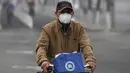 Seorang pria mengenakan masker mengendarai sepedanya di jalan pada hari yang tercemar polusi udara di Beijing, China (2/4). (AFP Photo/Fred Dufour)
