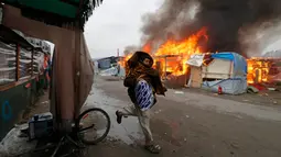 Seorang imigran berjalan melewati kobaran api di pengungsian imigran "Jungle", di kota pelabuhan Calais, Prancis (26/10). Pengosongan kamp ini sempat mendapat penolakan dari beberapa imigran. (REUTERS/Philippe Wojazer)