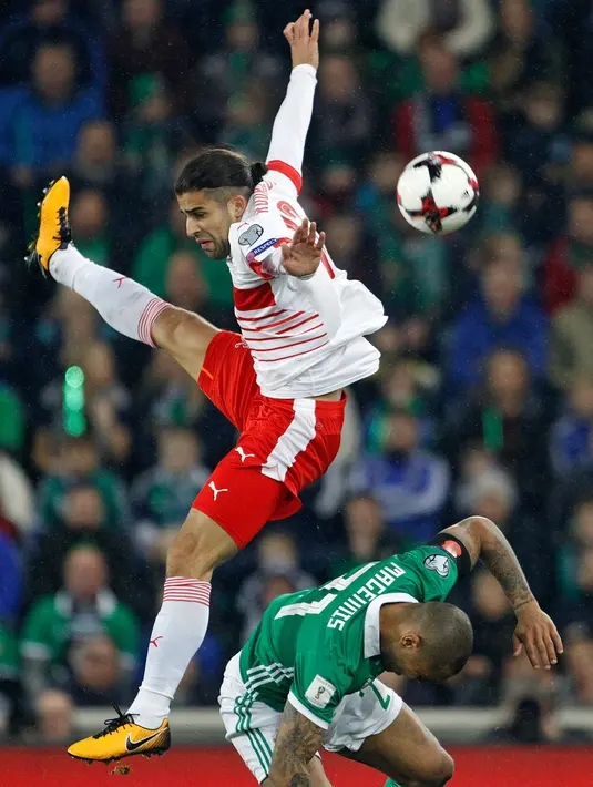 Pemain Swiss, Ricardo Rodriguez berada di atas pemain Irlandia Utara, Josh Magennis untuk merebut bola pada leg pertama playoff Piala Dunia 2018 di Windsor Park, Jumat (10/11). Bermain di kandang lawan, Swiss menang tipis 1-0. (AP/Peter Morrison)