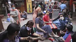 Perempuan yang mengenakan masker mendapatkan desain henna di tangan mereka pada malam festival Karva Chauth di New Delhi, India, Selasa (3/11/2020). Ini adalah festival untuk memulai bulan baru di bulan November di mana para istri akan berpuasa untuk suami-suami mereka. (AP Photo/Manish Swarup)