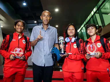 Pemain Timnas Indonesia, Laita Roati (kiri), Viny Silfianus (kedua kanan), Reva Octaviani (kanan), dan pelatih Satoru Mochizuki (kedua kiri) berpose dengan membawa trofi Piala AFF Wanita 2024 dan penghargaan individu (kiper terbaik dan pemain terbaik) saat mendarat di Gedung VVIP Terminal 3 Bandara Soekarno Hatta, Tangerang, Jumat (06/12/2024). (Bola.com/Bagaskara Lazuardi)