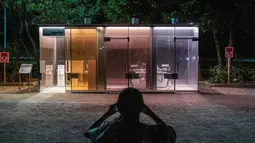 Seorang wanita mengambil foto toilet transparan di Haru-no-Ogawa Community Park di distrik Shibuya, Tokyo (19/8/2020). Toilet ini dirancang oleh Shigeru Ban dimana dinding luar kacanya akan berubah menjadi buram ketika kuncinya ditutup. (AFP Photo/Philip Fong)