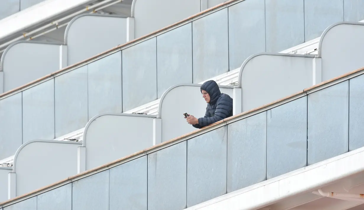 Penumpang bermain ponsel saat dikarantina di balkon di atas kapal pesiar Diamond Princess di Daikoku Pier Cruise Terminal di Yokohama (7/2/2020). Kementerian Kesehatan Jepang mengonfirmasi 41 penumpang kapal pesiar itu positif terinfeksi virus Corona. (AFP/Jiji Press)