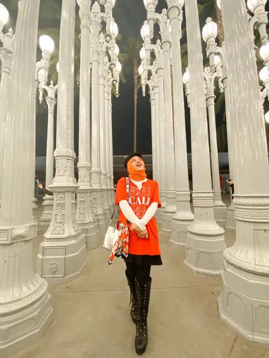 Sajidah Halilintar berpose dengan outfit bernuansa oranye. Ia mengenakan manset putih yang ditumpuknya dengan kaus lengan pendek berwarna oranye, rok hitam, dengan legging hitam, dan high boots yang juga berwarna hitam. Sajidah menambahkan hijau oranye dan topi hitam. [Foto: Instagram/sajidahhalilintar]