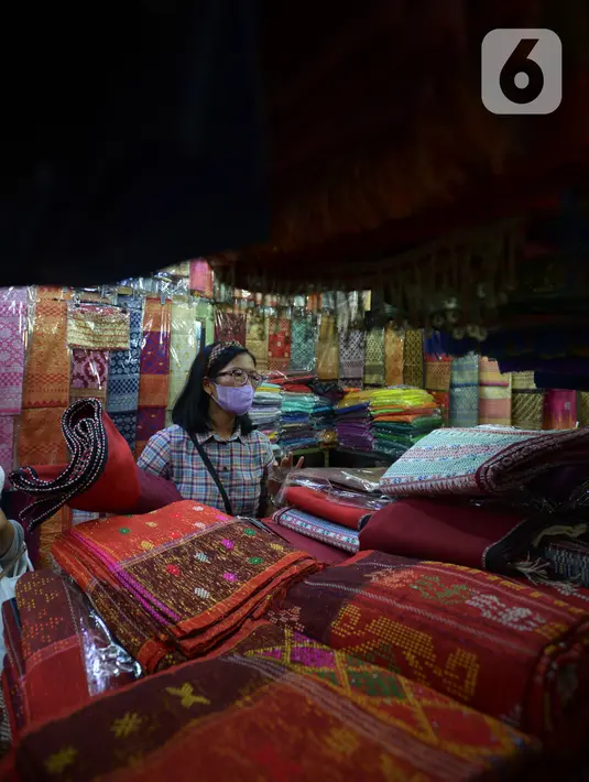 Aktivitas jual beli kain ulos di pasar proyek Senen, Jakarta, Kamis (21/10/2021). Sejak status PPKM turun dari level 3 menjadi level 2, pengunjung ramai mendatangi toko membeli kain ulos untuk upacara pernikahan adat dengan kisaran harga dari Rp. 500.000 hingga jutaan rupiah. (merdeka.com/Imam Buhor