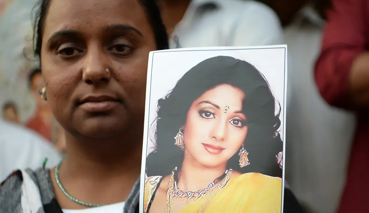 Seorang wanita memegang foto aktris Bollywood Sridevi Kapoor saat berdiri di luar rumah sang idola jelang pemakamannya, Mumbai, India, Rabu (28/2). (PUNIT PARANJPE/AFP)