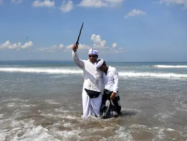 Seorang pria memegang keris saat sembahyang upacara Melasti di pantai Petitenget dekat Denpasar, di pulau resor Bali, Indonesia pada 19 Maret 2023. (AFP/SONNY TUMBELAKA)