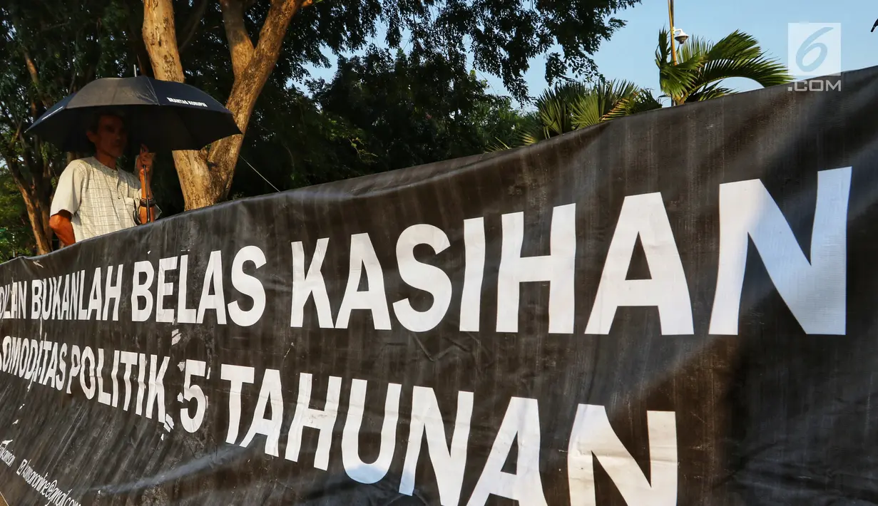 Aktivis JSKK membentangkan spanduk saat menggelar aksi Kamisan ke-589 di depan Istana Merdeka, Jakarta, Kamis (20/6/2019). Dalam aksinya, JSKK meminta Presiden Joko Widodo memegang teguh komitmen untuk menyelesaikan pelanggaran HAM berat masa lalu. (Liputan6.com/Johan Tallo)
