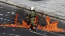 Polisi anti huru-hara melwati jalanan yang terbakar api di Athena, Yunani, (12/11/2015). Para Demonstran juga melakukan aksi mogok kerja selama 24 jam. (REUTERS/Yannis Behrakis)
